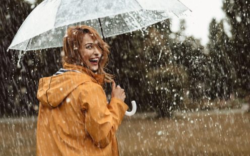 Cheerful pretty girl holding umbrella while strolling outside. She is turning back and looking at camera with true delight and sincere smile. Copy space in right side