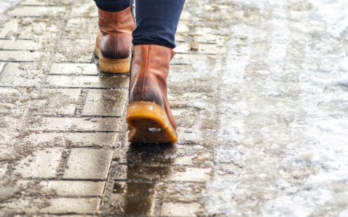 Walk on wet melted ice pavement. Back view on the feet of a man walking along the icy pavement. Pair of shoe on icy road in winter. Abstract empty blank winter weather background