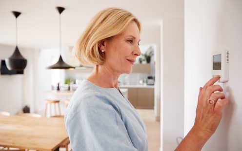 Close Up Of Mature Woman Adjusting Central Heating Temperature At Home On Thermostat