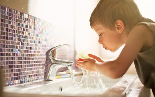 Little boy drinking tap water. Little boy aged 4 is drinking tap water in sunlit bathroom.
