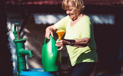 Senior woman in her garden outdoors preparing to water the plants, caring, love the nature, backyard